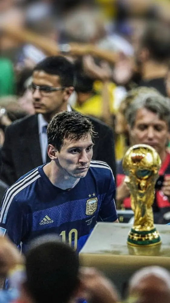 Messi in Argentina's navy away shirt walking past the World Cup trophy at the Maracanã in 2014